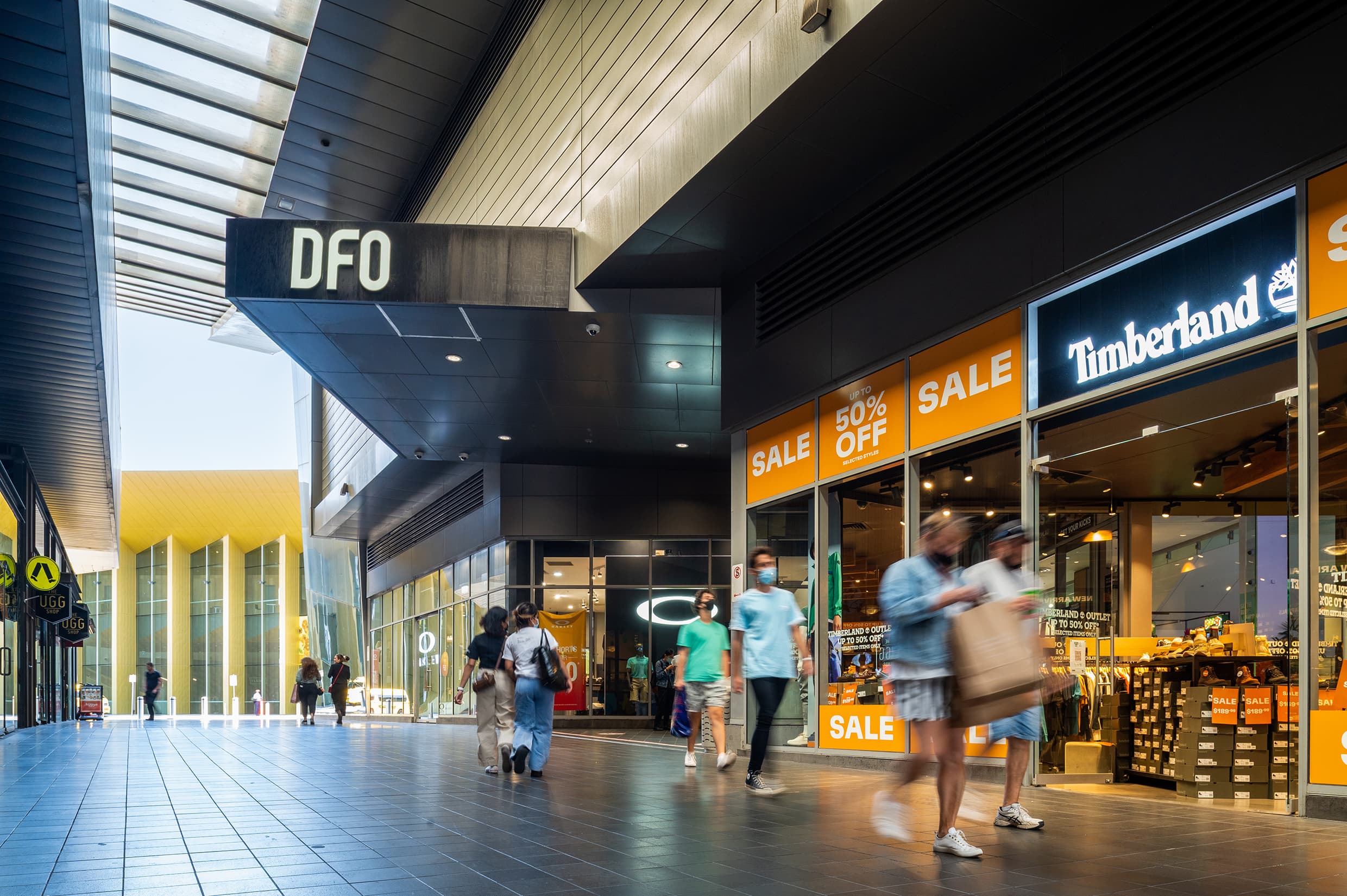 Shoppers walk along a shopping centre avenue with black floor and roof covering