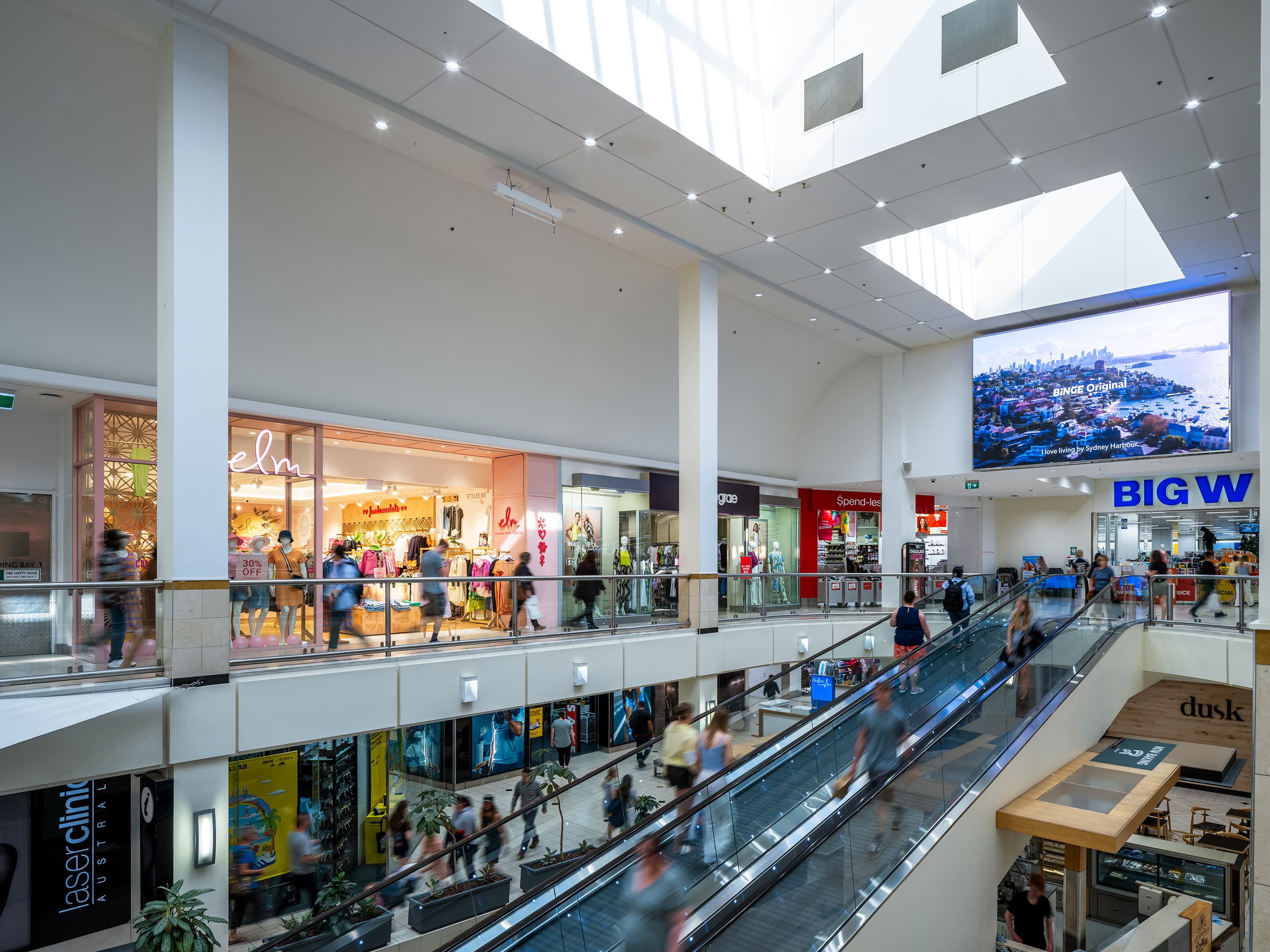 People walking through a large and airy shopping centre atrium with travelator