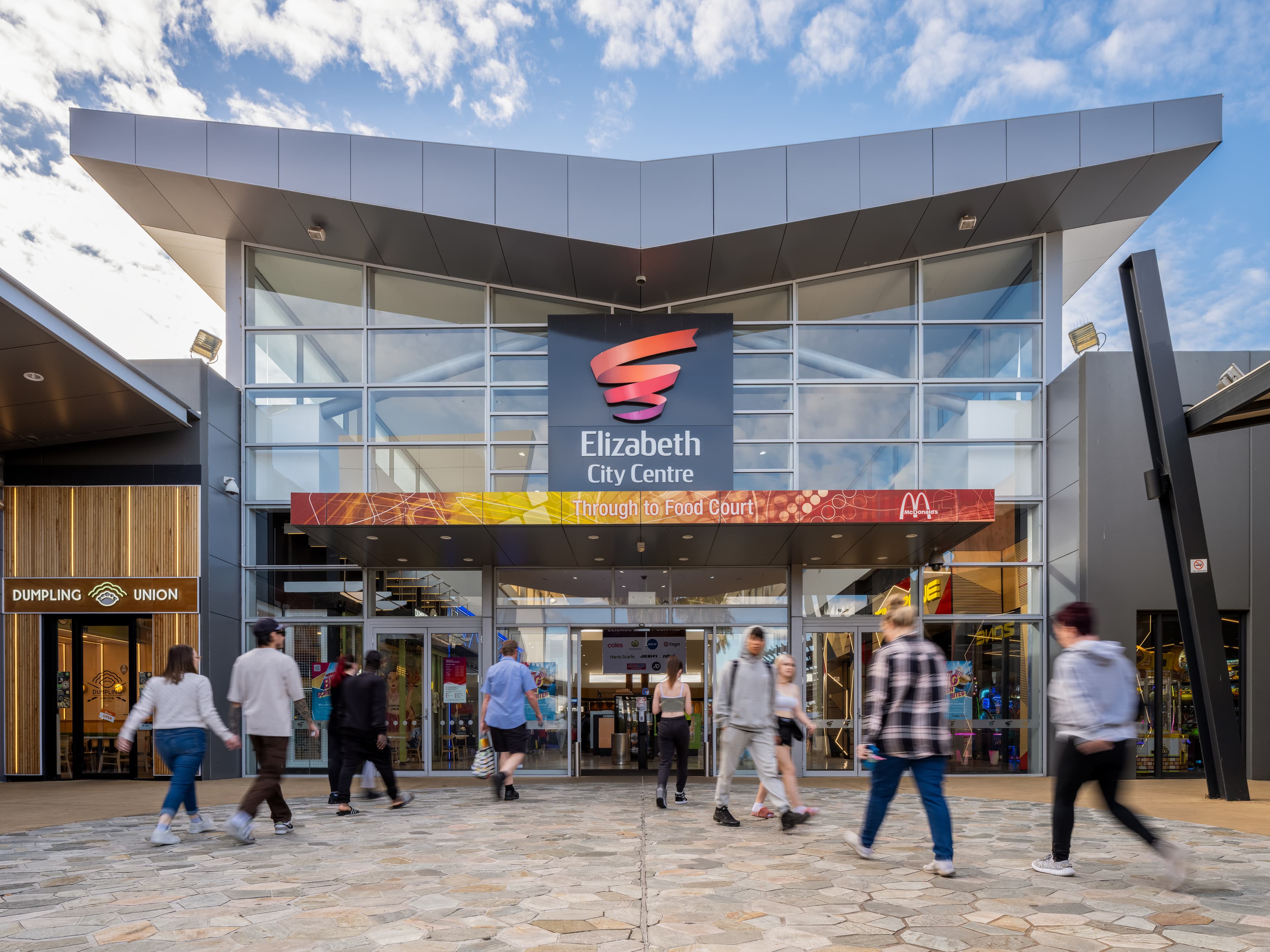 Glass fronted entrance to Elizabeth City Centre shopping centre with large sign and people walking inside